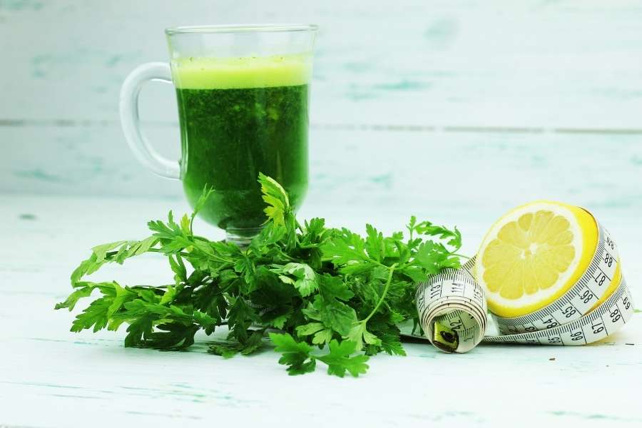 Jus vert aux herbes fraîches avec du persil, un citron et un mètre ruban, illustrant les boissons minceur naturelles et détoxifiantes.