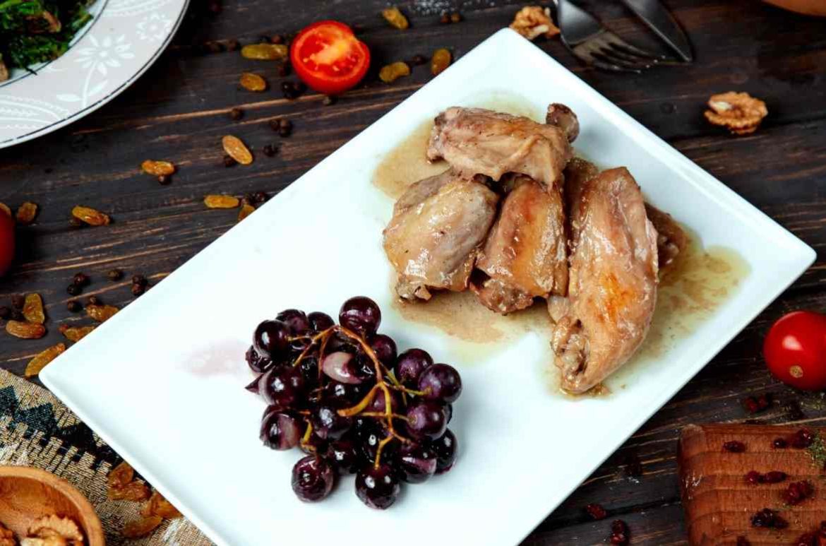 Assiette de confit de canard servi avec des raisins poêlés sur une table en bois